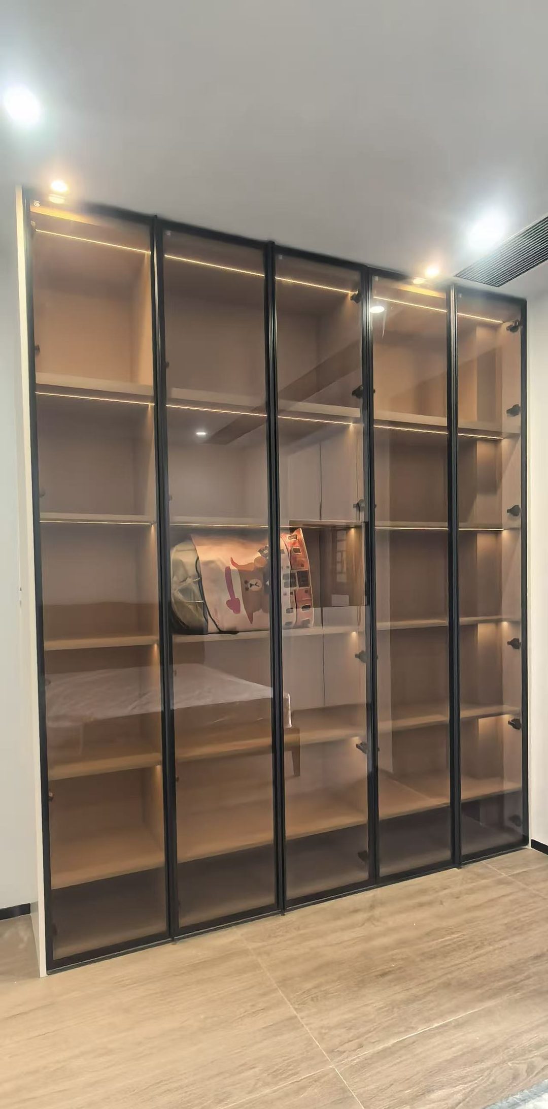 通顶展示柜 · 黑框茶玻+暖光灯带,床尾一面墙的气氛担当